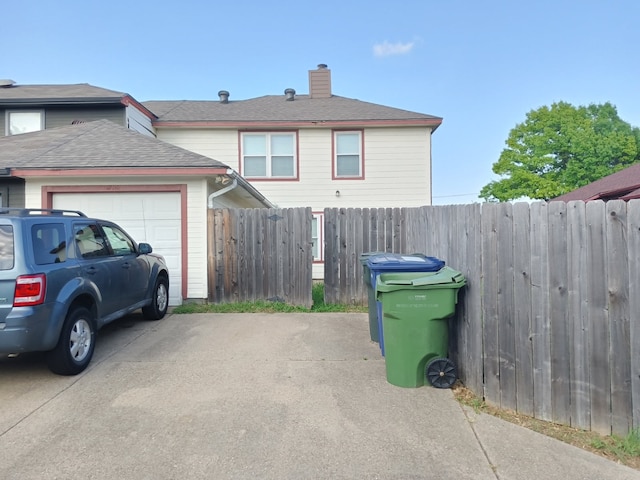 exterior space with driveway, a chimney, roof with shingles, a garage, and fence