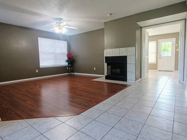 unfurnished living room featuring tile patterned flooring, a fireplace, baseboards, a textured ceiling, and a ceiling fan