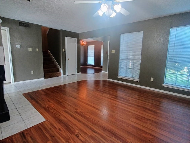 unfurnished living room featuring ceiling fan with notable chandelier, stairs, wood finished floors, and visible vents