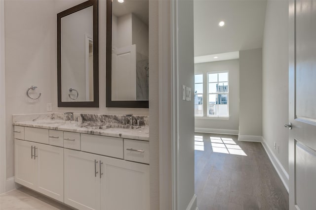 bathroom with double vanity, baseboards, a sink, and wood finished floors
