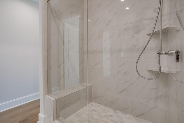 full bath featuring baseboards, a marble finish shower, and wood finished floors