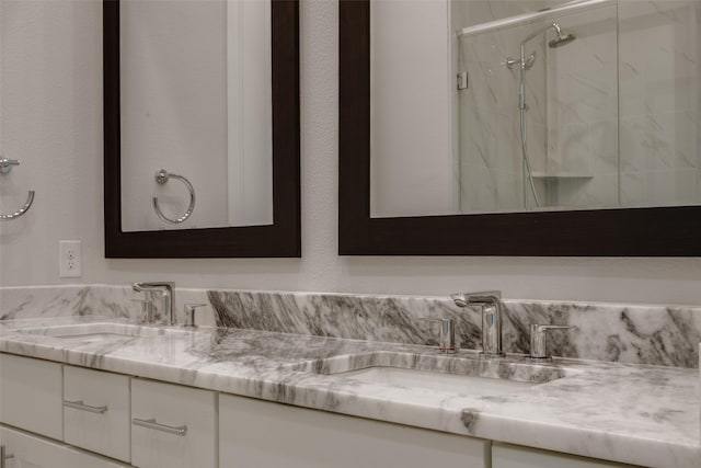 full bath with double vanity, a marble finish shower, and a sink