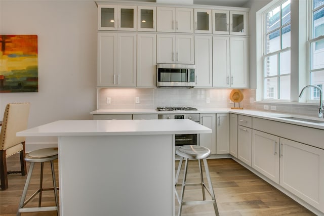 kitchen featuring a breakfast bar area, light wood-type flooring, light countertops, stainless steel microwave, and a sink