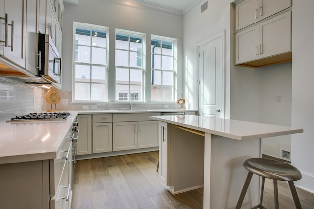 kitchen with backsplash, visible vents, crown molding, light wood-type flooring, and stainless steel appliances