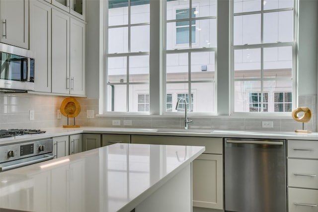 kitchen with backsplash, appliances with stainless steel finishes, a sink, light countertops, and glass insert cabinets