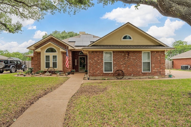 ranch-style home featuring roof with shingles, brick siding, a front yard, roof mounted solar panels, and cooling unit