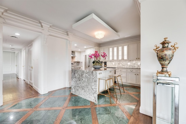 kitchen with light stone counters, ornamental molding, freestanding refrigerator, and backsplash