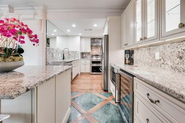 kitchen featuring light stone countertops, wine cooler, ornamental molding, stainless steel appliances, and white cabinetry