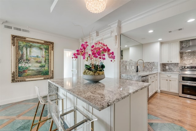 kitchen featuring visible vents, light stone countertops, wall chimney range hood, white cabinetry, and double oven range