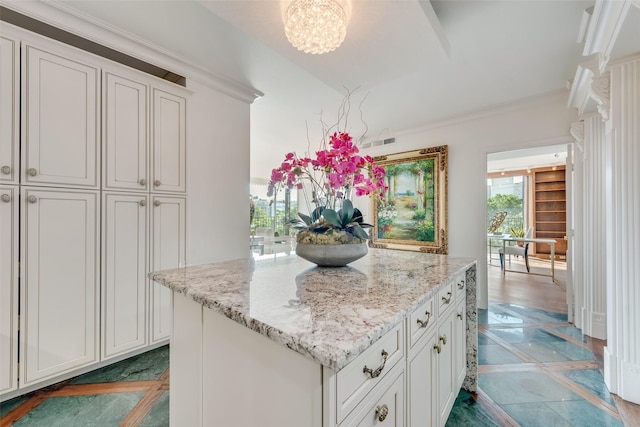 kitchen with white cabinetry, a notable chandelier, a kitchen island, and light stone countertops