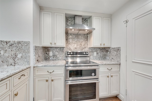 kitchen with wall chimney range hood, range with two ovens, light stone countertops, and tasteful backsplash