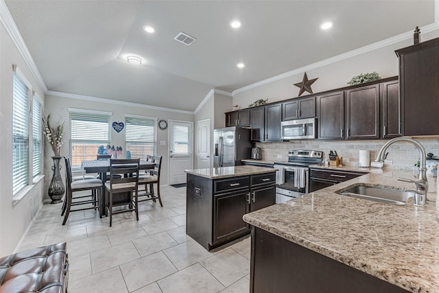kitchen featuring decorative backsplash, a kitchen island, appliances with stainless steel finishes, a sink, and light stone counters