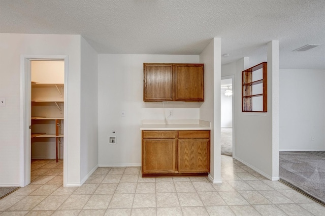 kitchen with light countertops, a textured ceiling, brown cabinetry, baseboards, and visible vents