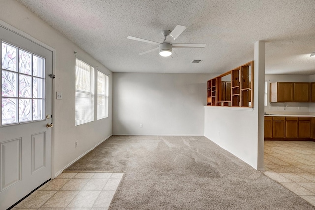 interior space with visible vents, light carpet, baseboards, a textured ceiling, and a ceiling fan
