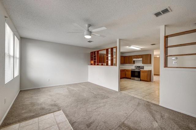 unfurnished living room with ceiling fan, a textured ceiling, light colored carpet, visible vents, and baseboards