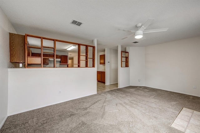 unfurnished room featuring visible vents, baseboards, ceiling fan, light colored carpet, and a textured ceiling