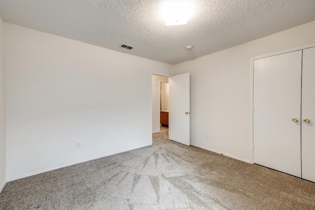 unfurnished bedroom with a textured ceiling, visible vents, baseboards, a closet, and carpet