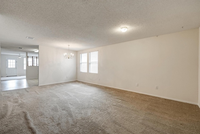 spare room featuring carpet floors, a textured ceiling, a chandelier, and a wealth of natural light