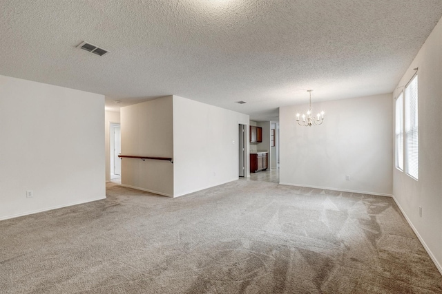 spare room featuring visible vents, light colored carpet, a textured ceiling, and a chandelier
