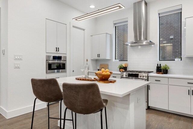 kitchen featuring tasteful backsplash, a breakfast bar, stainless steel appliances, wall chimney exhaust hood, and dark wood-type flooring