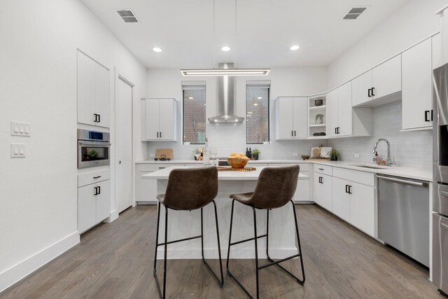 kitchen featuring a kitchen breakfast bar, a kitchen island, a sink, stainless steel appliances, and wall chimney exhaust hood