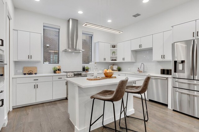kitchen featuring appliances with stainless steel finishes, a sink, wall chimney exhaust hood, a kitchen bar, and backsplash