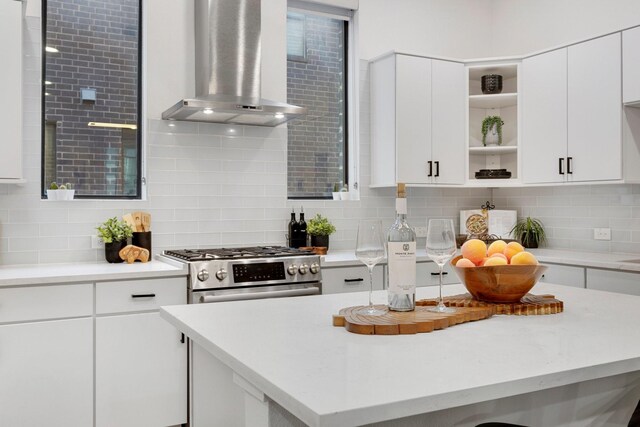 kitchen with wall chimney range hood, light countertops, decorative backsplash, and open shelves