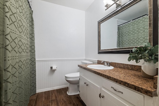 bathroom featuring wood finished floors, a wainscoted wall, toilet, vanity, and curtained shower