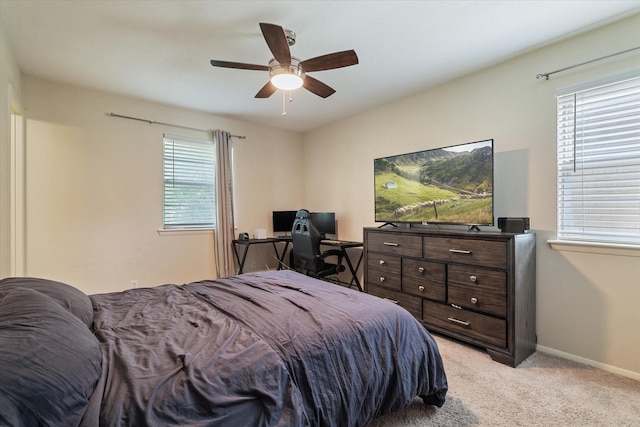 bedroom with light colored carpet, a desk, baseboards, and a ceiling fan
