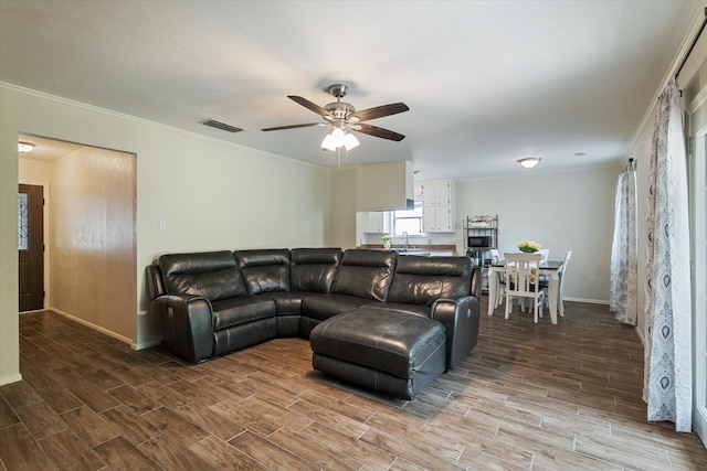 living area with a ceiling fan, wood finished floors, crown molding, and baseboards