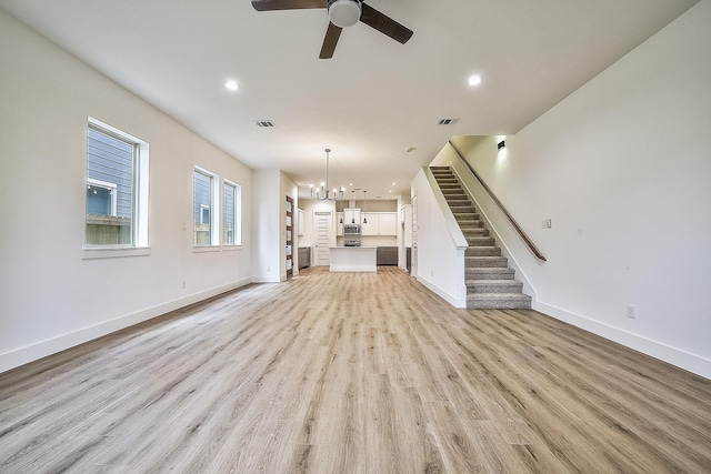 unfurnished living room with stairs, baseboards, light wood-type flooring, recessed lighting, and ceiling fan with notable chandelier