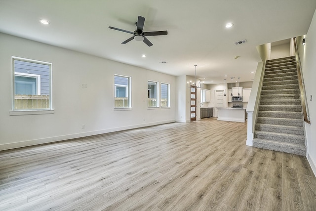 unfurnished living room featuring stairway, baseboards, ceiling fan with notable chandelier, and light wood-style floors
