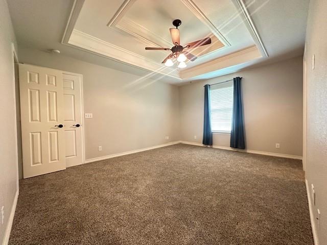 empty room with a raised ceiling, baseboards, carpet, and a ceiling fan