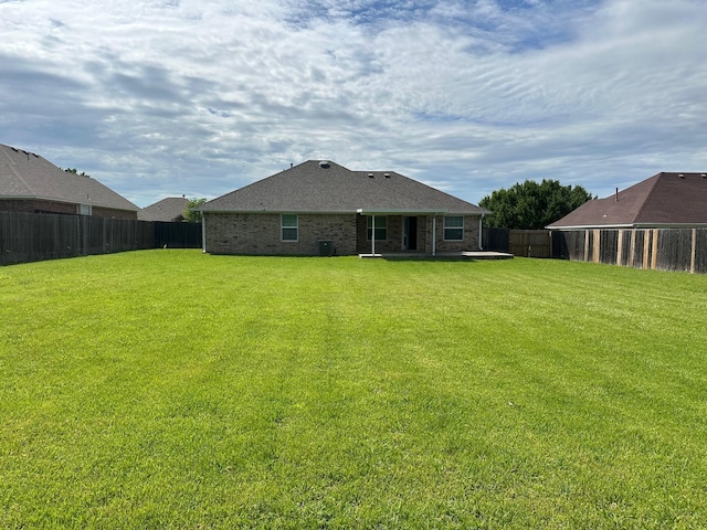 rear view of property with roof with shingles, brick siding, a fenced backyard, a patio area, and a yard