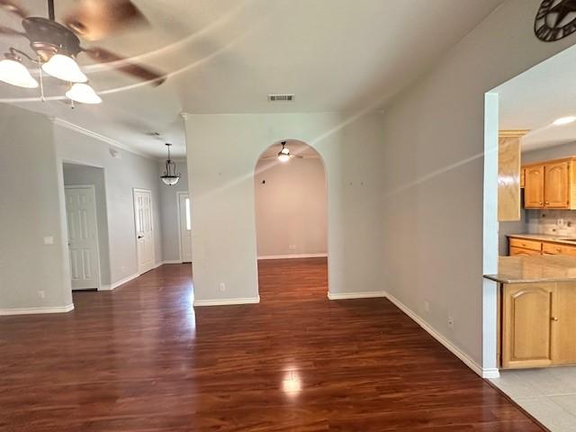 unfurnished living room featuring ceiling fan, visible vents, arched walkways, wood finished floors, and baseboards