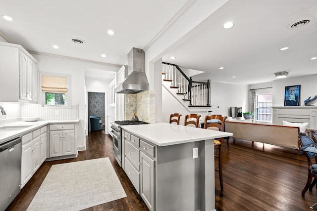 kitchen featuring a breakfast bar, wall chimney range hood, white cabinets, a sink, and stainless steel appliances