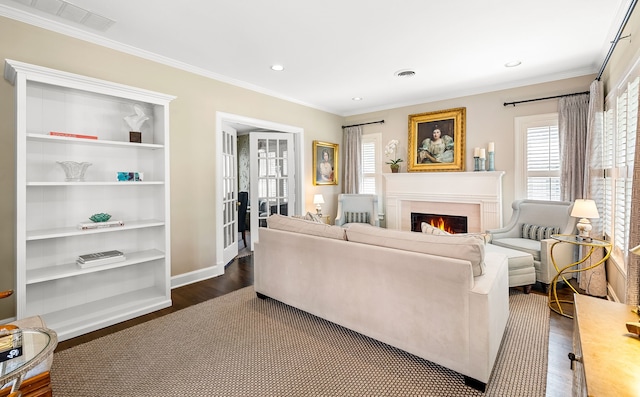 living area with a warm lit fireplace, dark wood finished floors, plenty of natural light, and visible vents