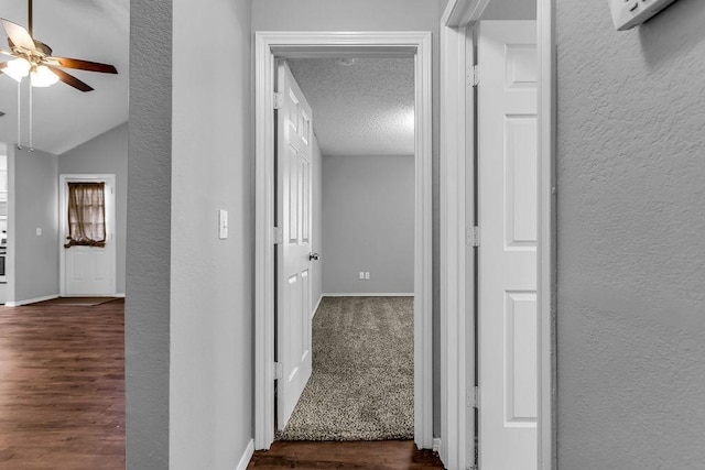 corridor featuring a textured wall, baseboards, and dark wood-type flooring