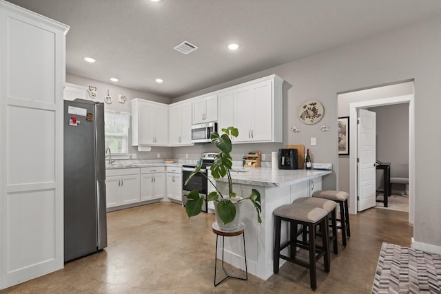 kitchen with a kitchen bar, finished concrete flooring, a peninsula, stainless steel appliances, and white cabinetry