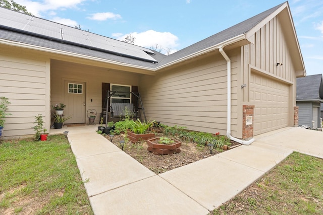 property entrance with concrete driveway, board and batten siding, roof with shingles, and solar panels