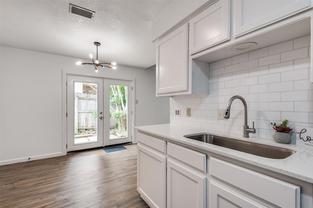 kitchen with backsplash, visible vents, wood finished floors, a sink, and a notable chandelier