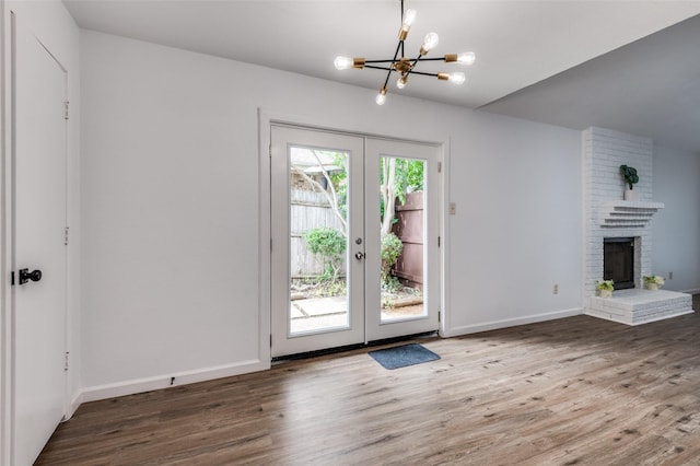 entryway with french doors, a brick fireplace, wood finished floors, baseboards, and a notable chandelier