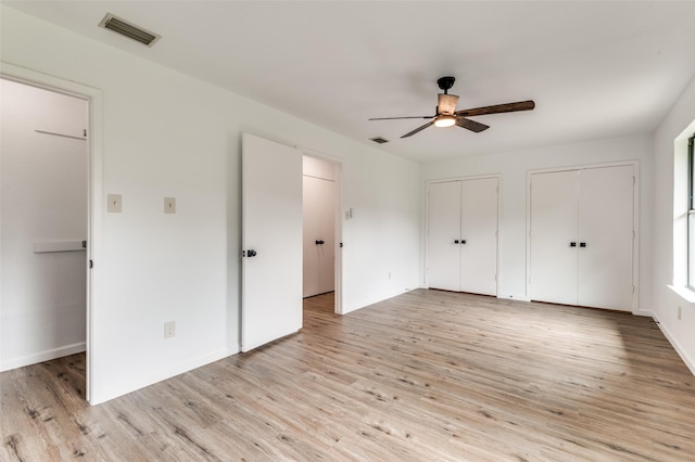 unfurnished bedroom with visible vents, baseboards, light wood finished floors, and two closets