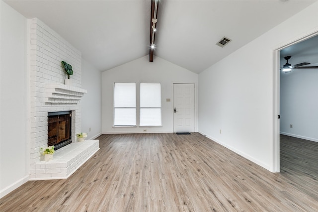 unfurnished living room with a ceiling fan, visible vents, a brick fireplace, wood finished floors, and vaulted ceiling with beams