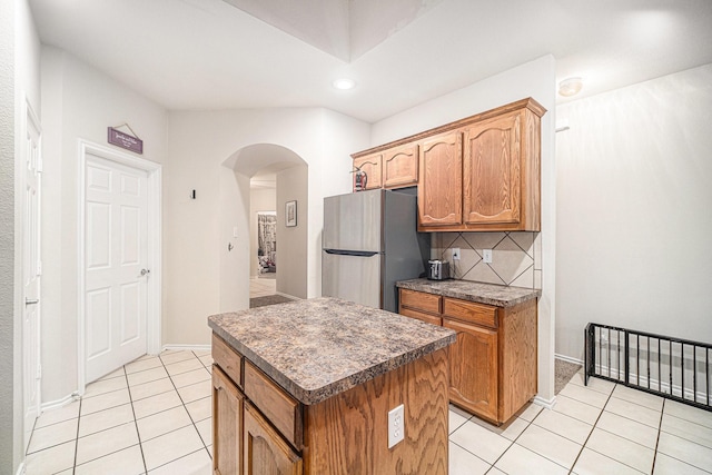kitchen with arched walkways, freestanding refrigerator, decorative backsplash, light tile patterned floors, and a kitchen island