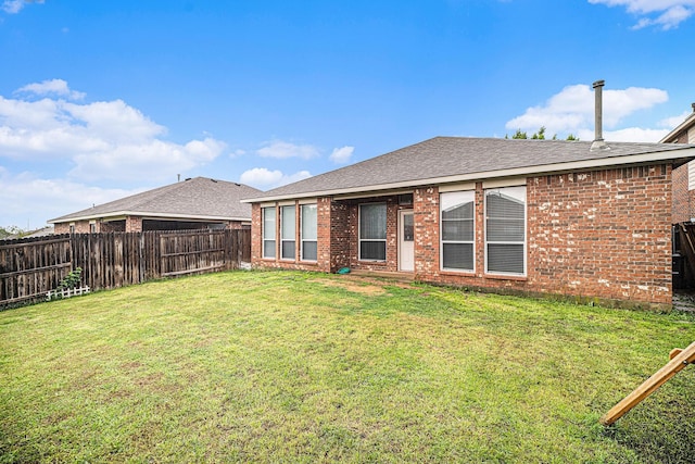 rear view of property featuring brick siding, a fenced backyard, a yard, and a shingled roof