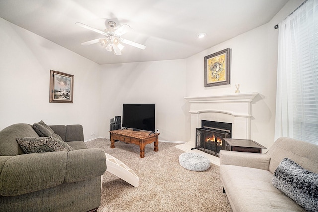 carpeted living area featuring baseboards, a ceiling fan, and a lit fireplace