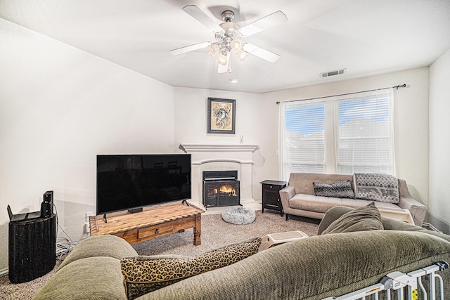 carpeted living room with visible vents, baseboards, ceiling fan, and a lit fireplace