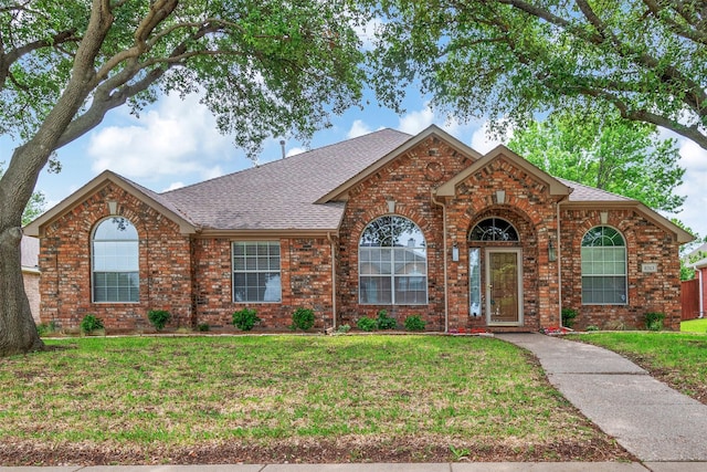 ranch-style house with a shingled roof, a front yard, and brick siding
