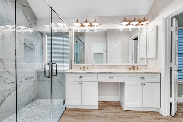 full bath featuring double vanity, a marble finish shower, a sink, and wood finished floors